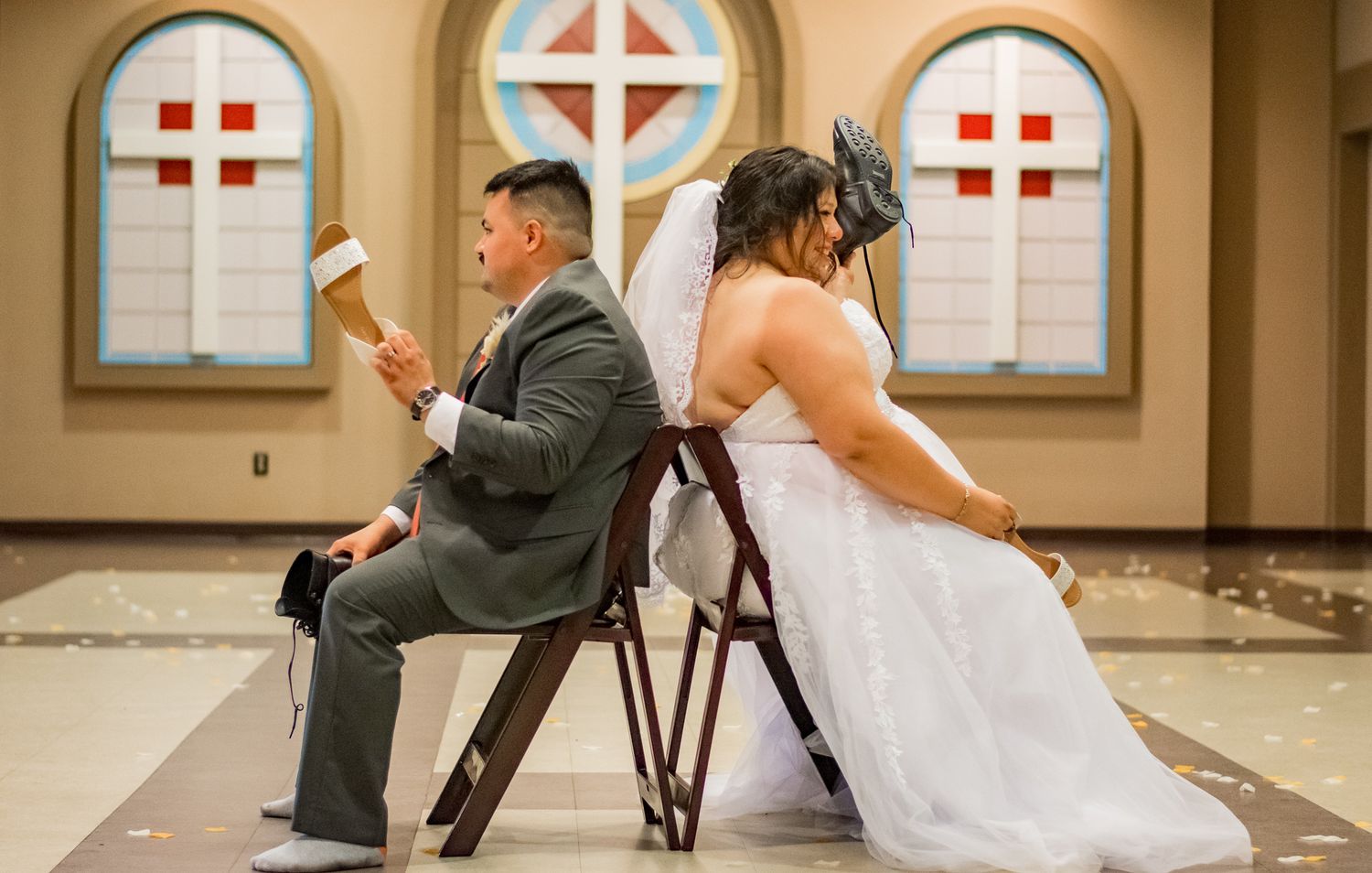 A playful wedding game with a couple sitting back to back in chairs at a church venue.