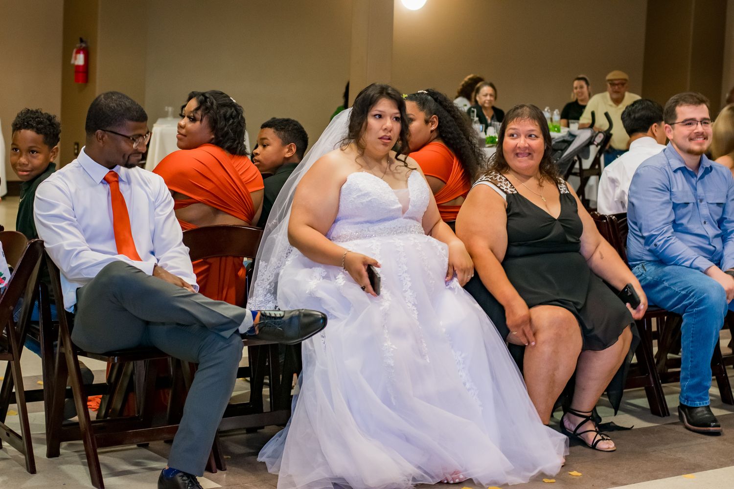 Wedding guests seated in formal attire at a reception with orange and black color scheme.