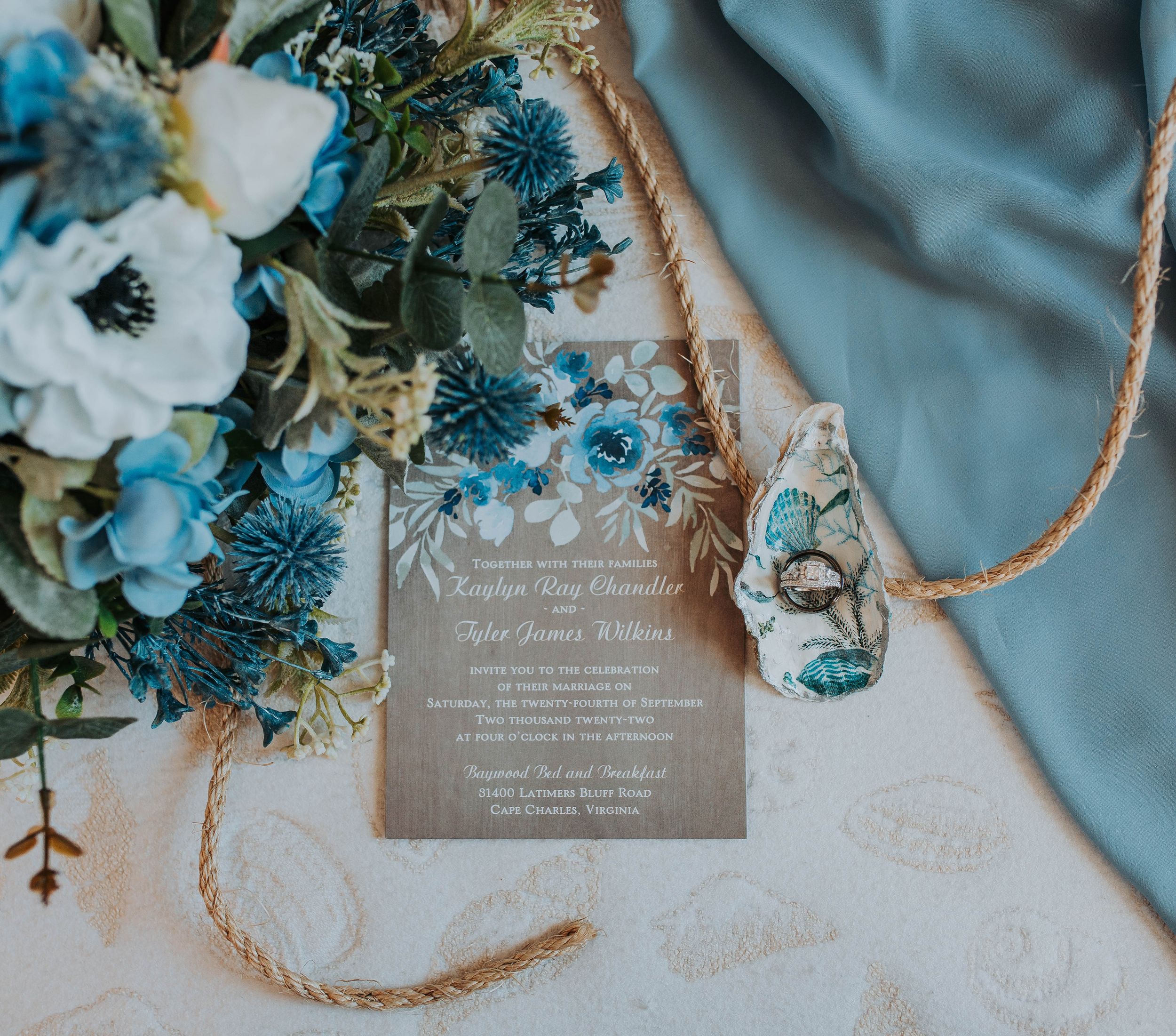 Rustic wedding invitation for Kayelyn and Tyler with blue floral bouquet and teal ribbon.