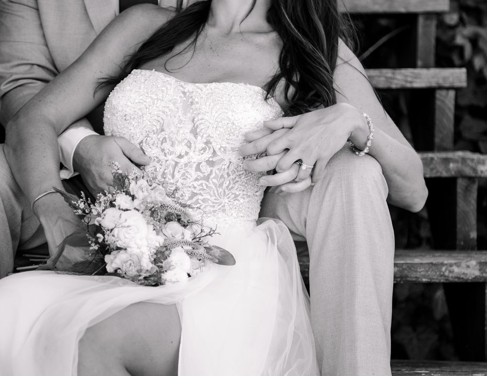 Black and white photo of bride and groom sitting together, bride holding a floral bouquet.