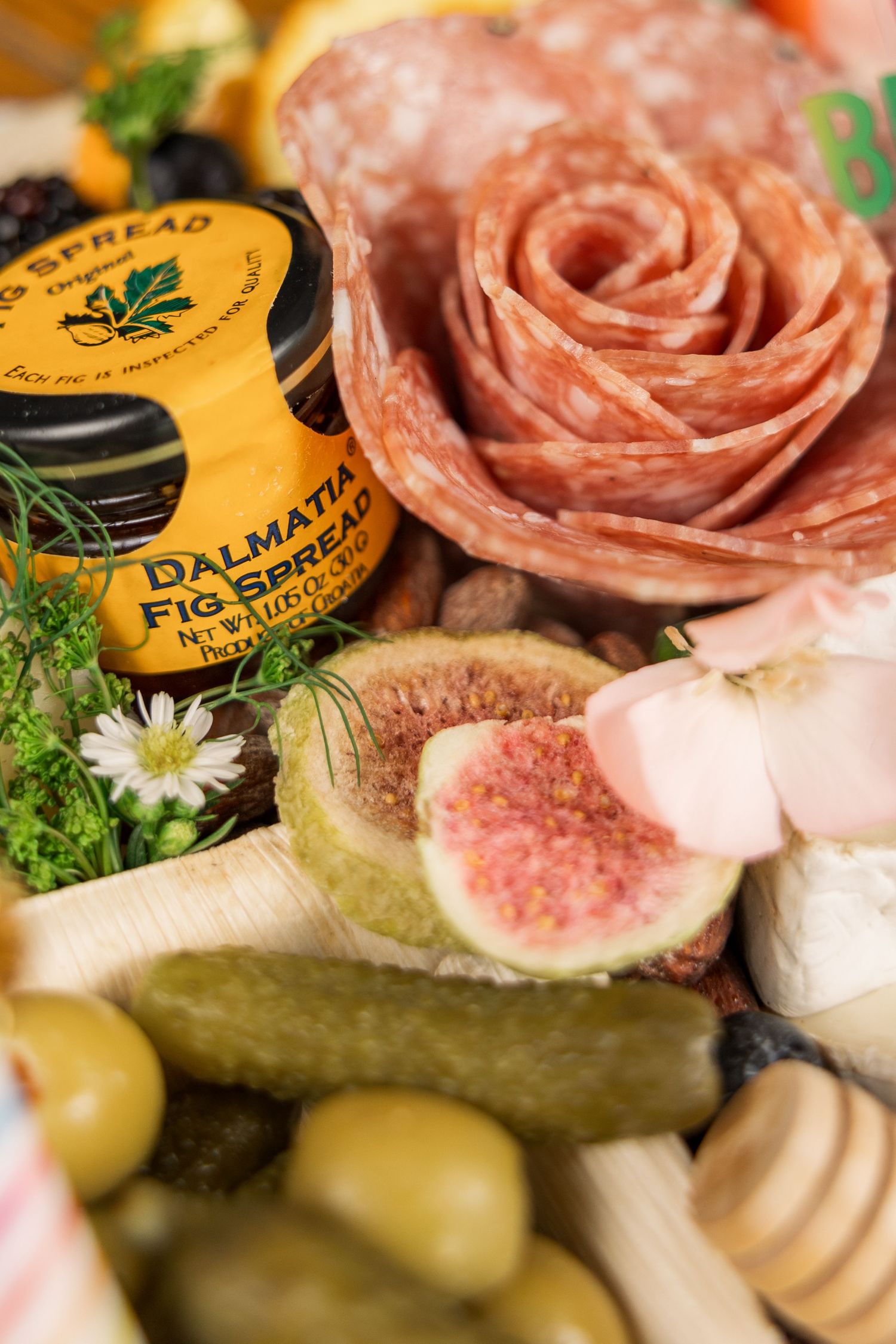 Close-up of fig spread jar, salami rose, and fresh figs on a charcuterie board.
