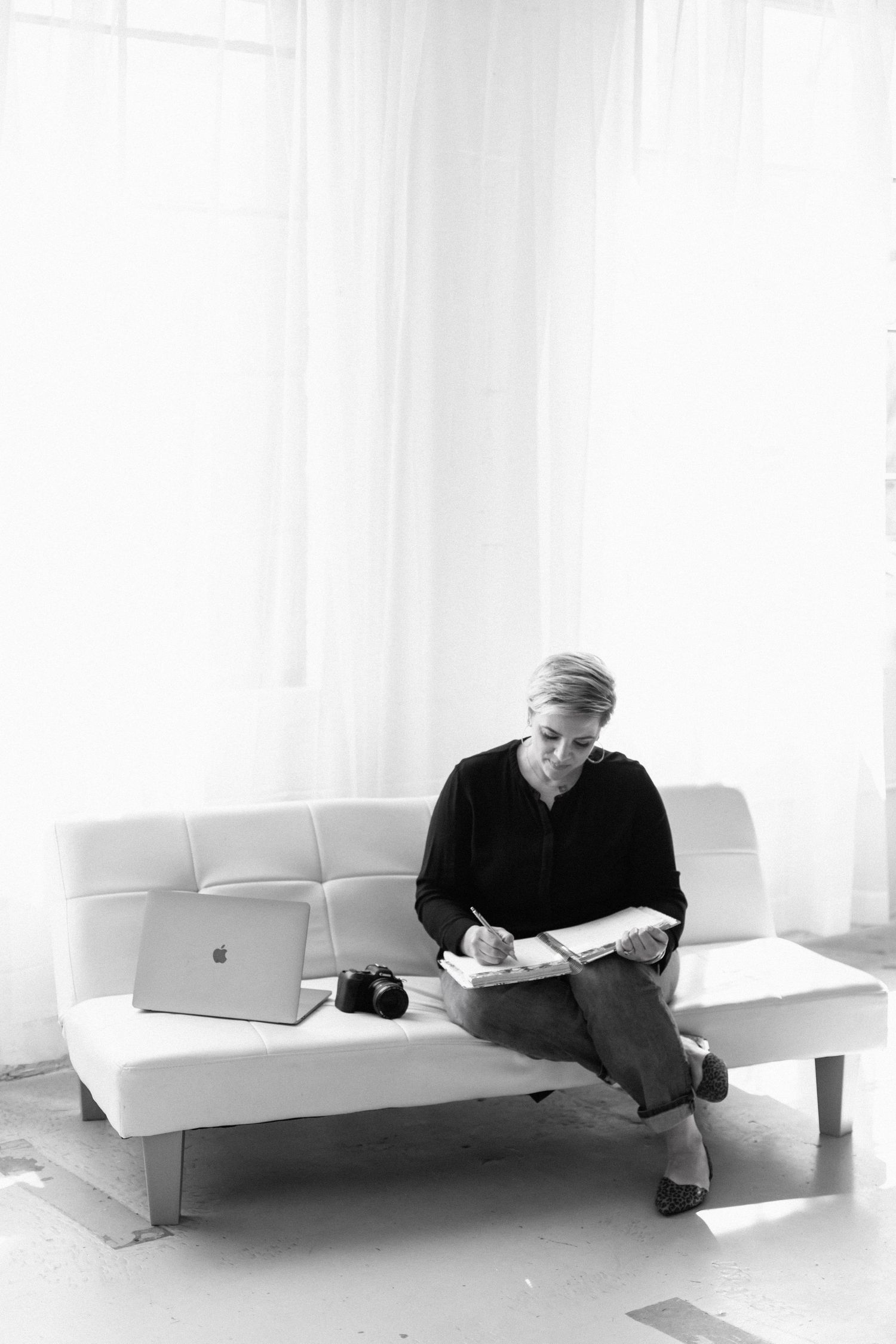Aly Darin sitting on couch writing in notebook with computer and camera. Beverly Hills, MI Senior photographer