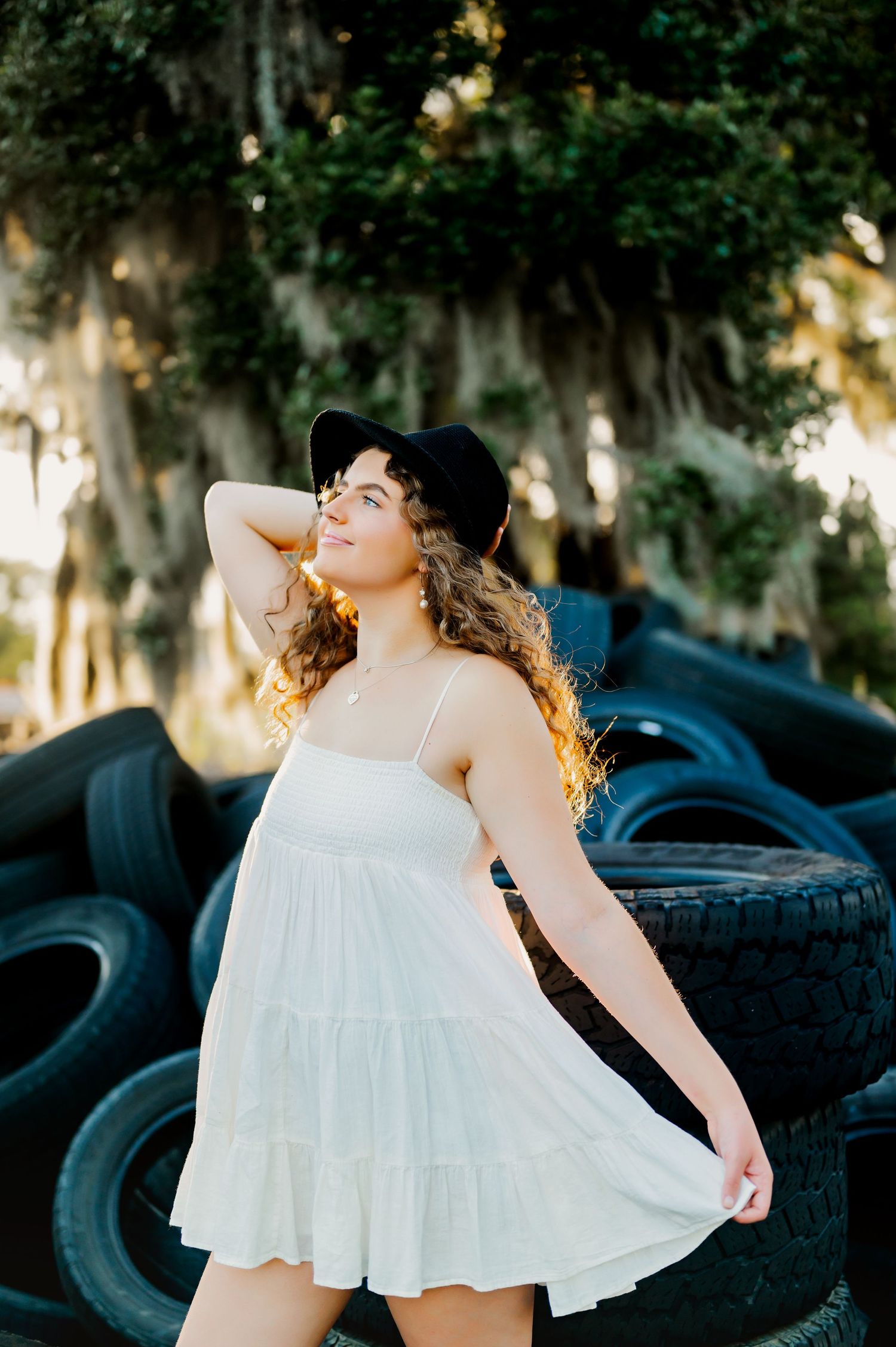 Sunlit portrait of woman in white dress posed by vintage tires.