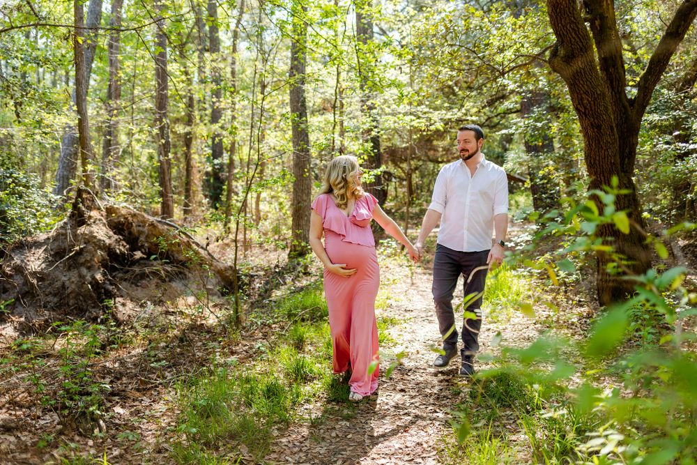 Expecting couple strolling together on wooded trail during sunny day.