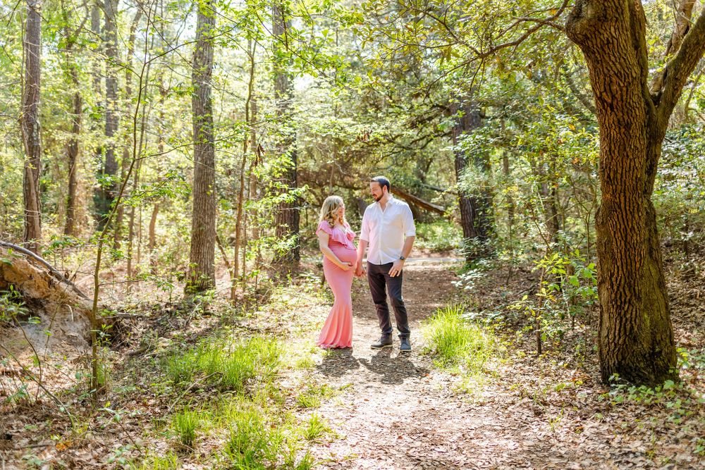 Couple sharing intimate moment on forest path during pregnancy photoshoot.