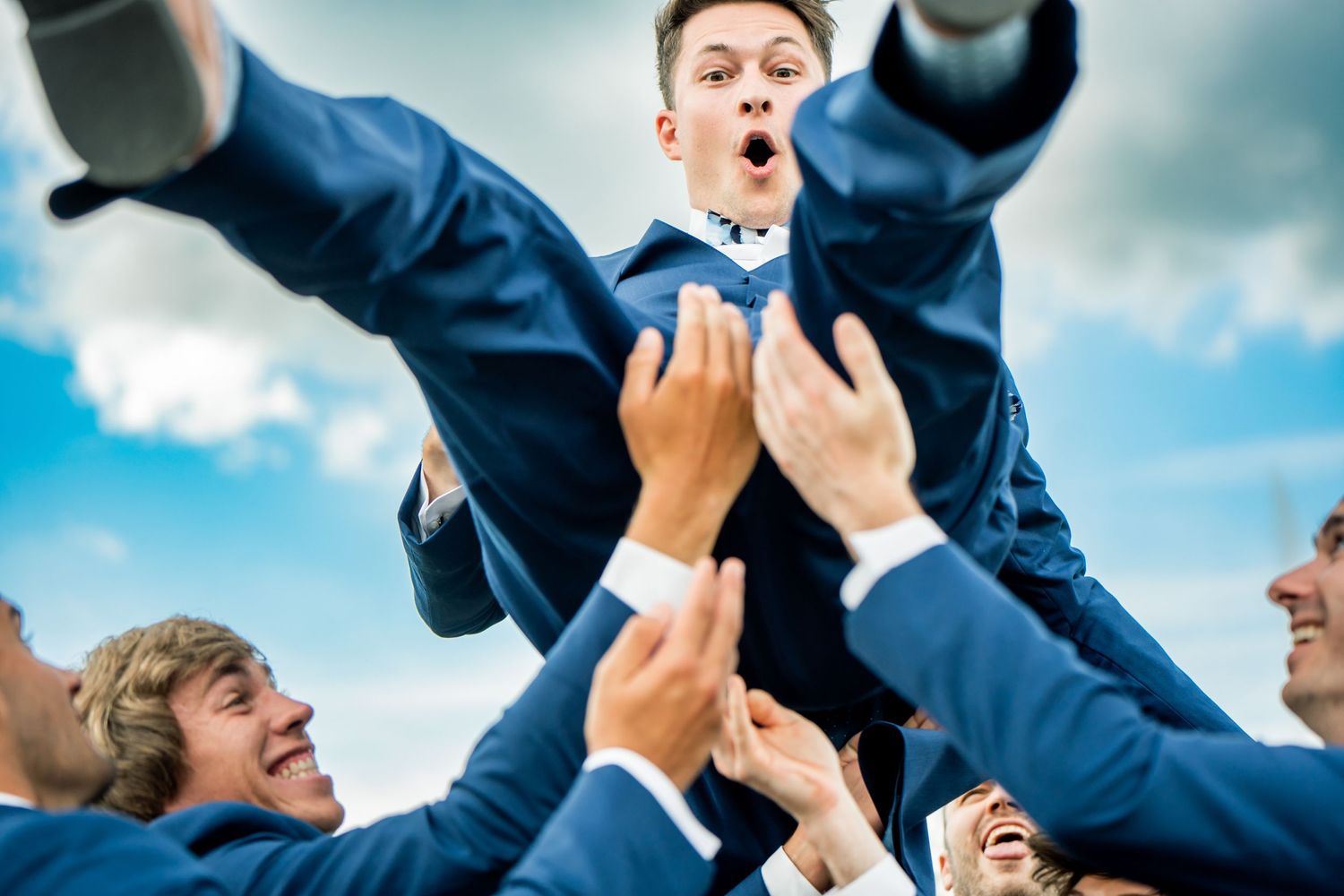 Groomsmen in navy suits celebrate with joyful jumping photo outdoors.