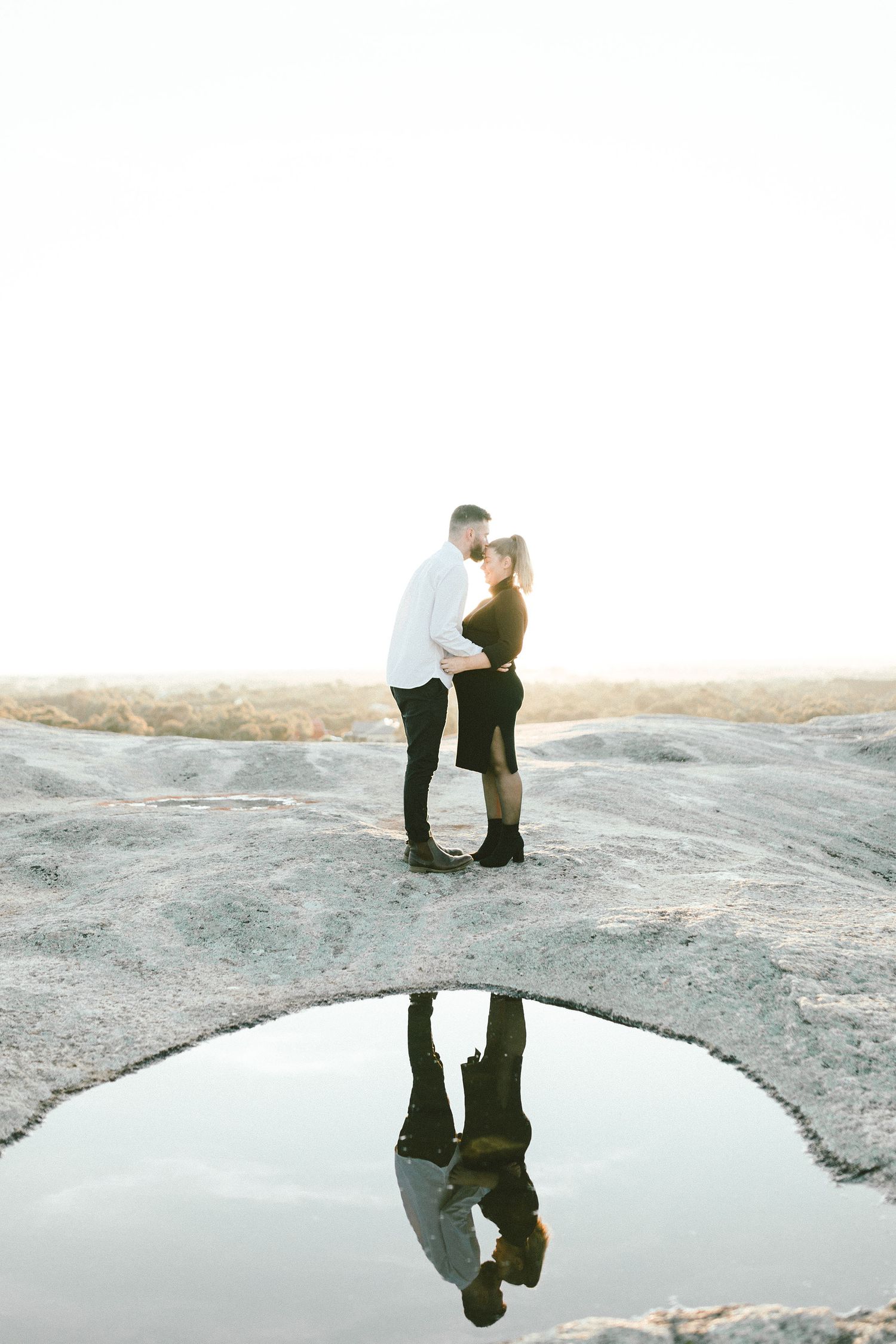 Couple embracing on rocky surface with their reflection in puddle below.