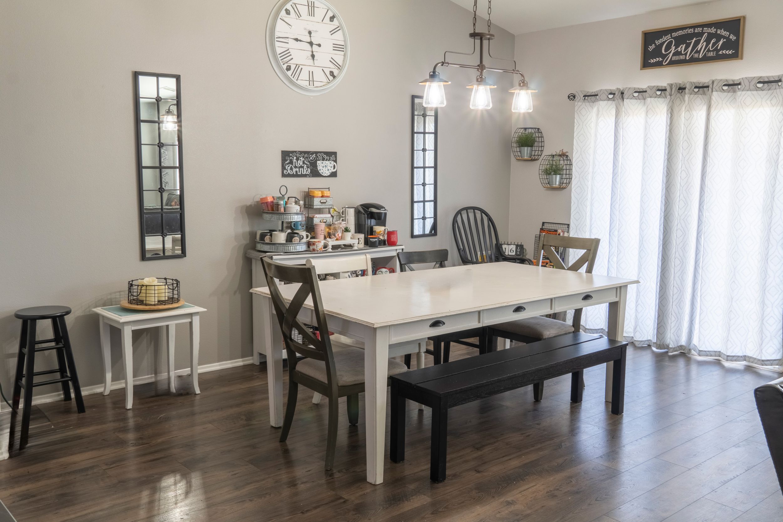 Farmhouse dining room with white table, bench, dark wood floors, pendant lighting, and large wall clock.