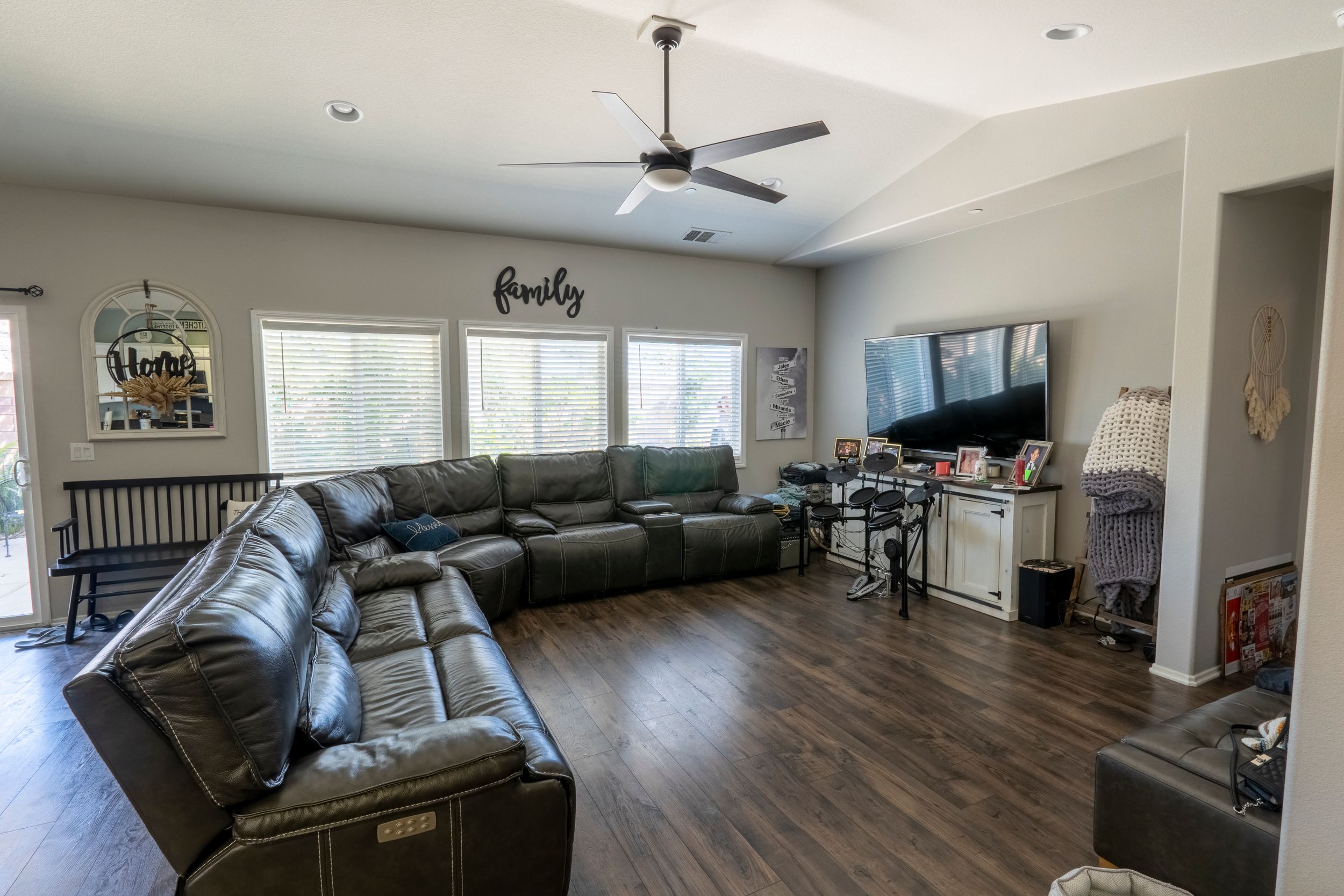 Spacious living room with large sectional sofa, ceiling fan, hardwood floors, and natural light from windows.
