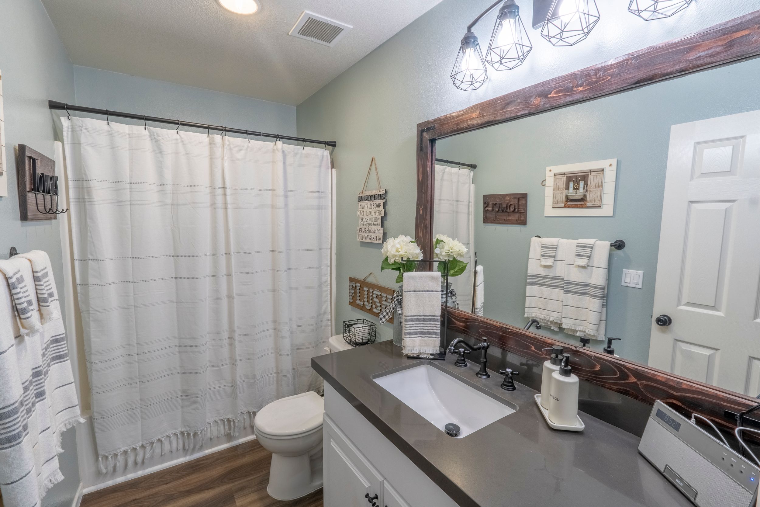 Modern farmhouse bathroom with wood-framed mirror, dark countertop vanity, and decorative pendant lighting.