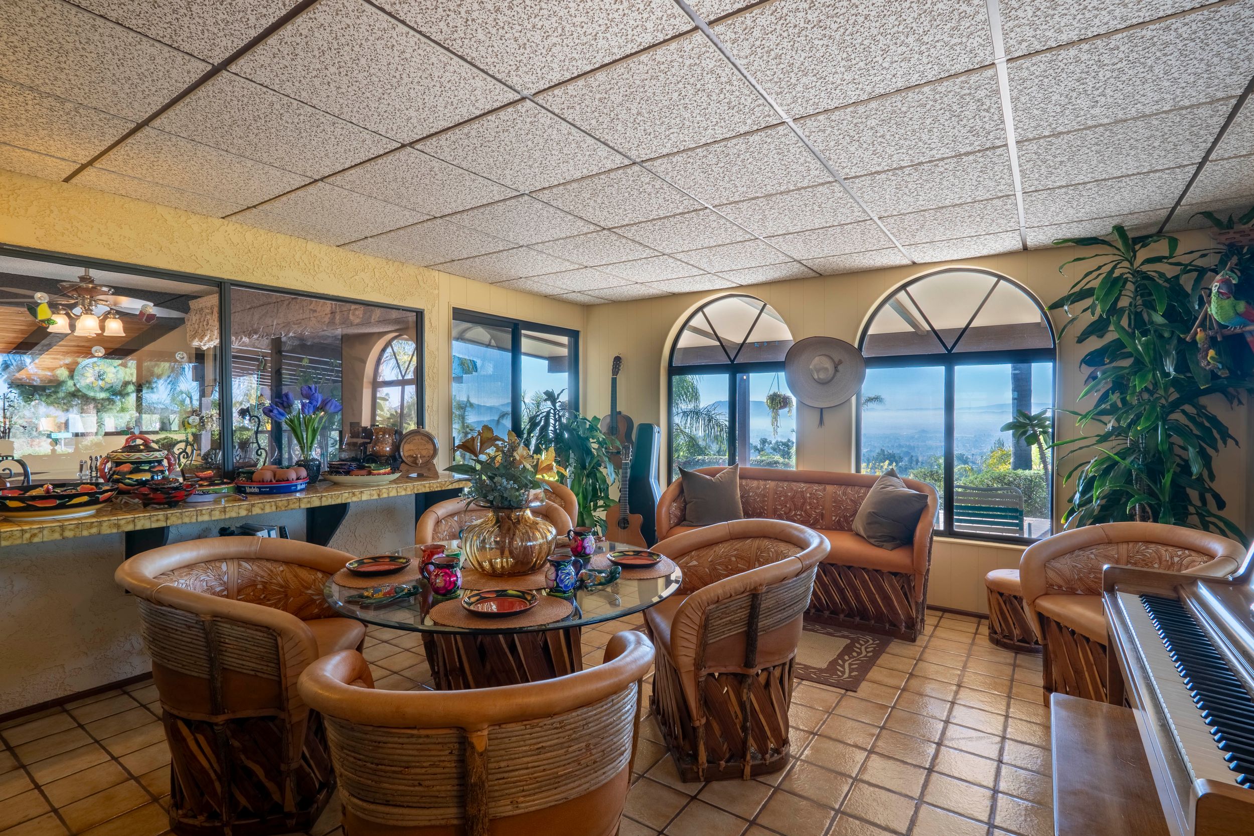 Bright dining area with rattan chairs, glass table, arched windows, and panoramic mountain views in a California home.