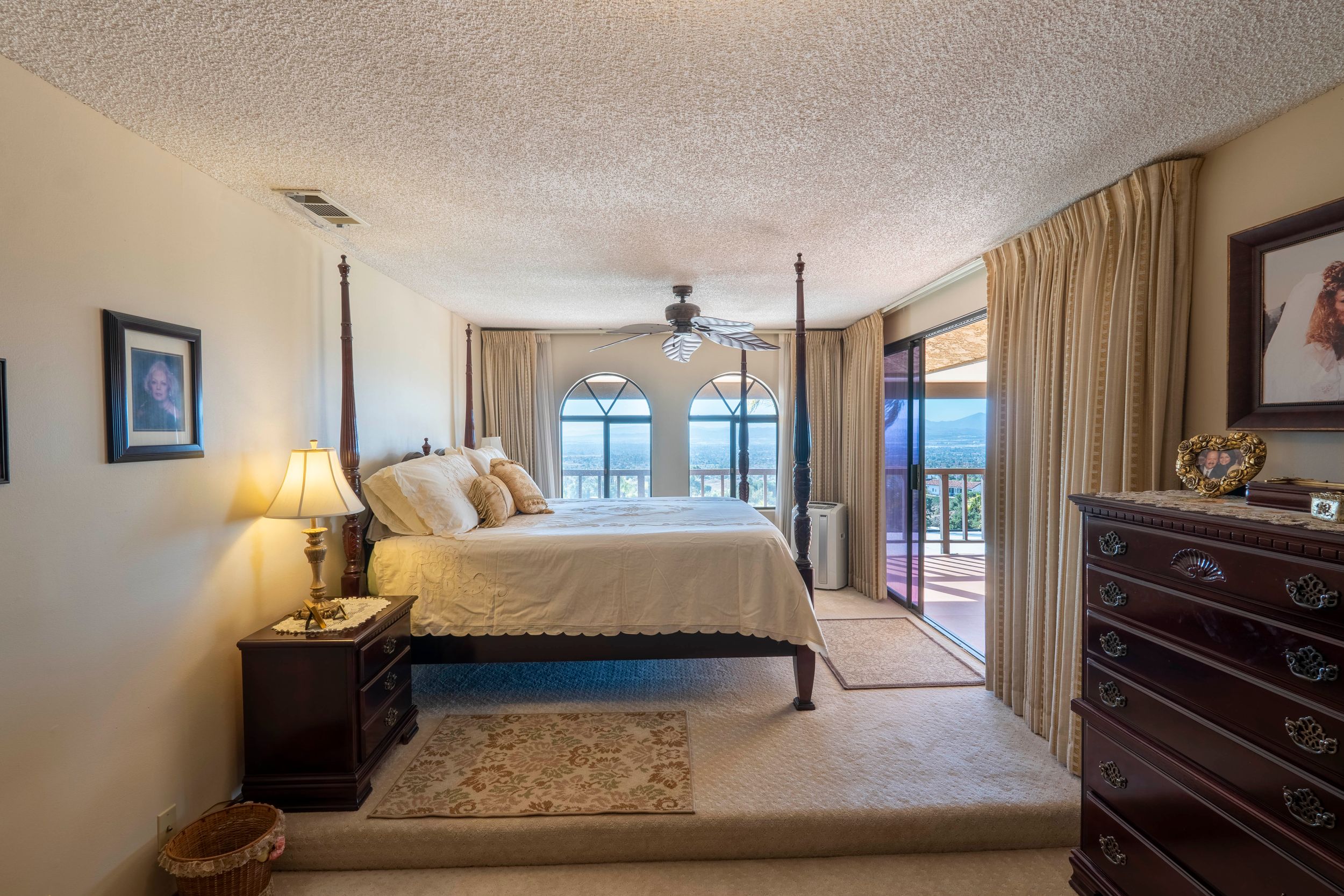Spacious master bedroom with four-poster bed, ceiling fan, carpet flooring, and sliding glass doors with ocean views.