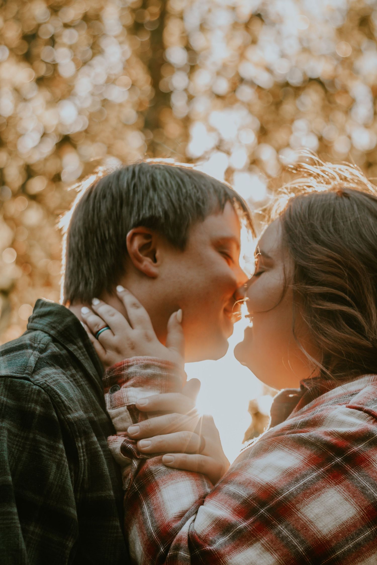 A couple shares a kiss bathed in warm golden bokeh light outdoors.