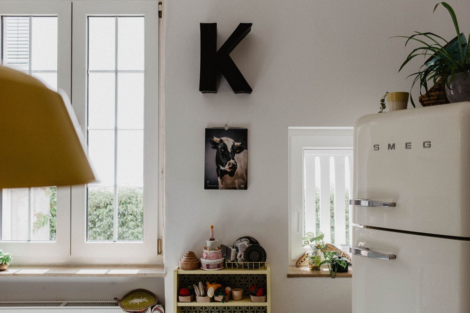 Stylish kitchen interior with retro SMEG refrigerator, yellow lamp and black letter K wall decor.
