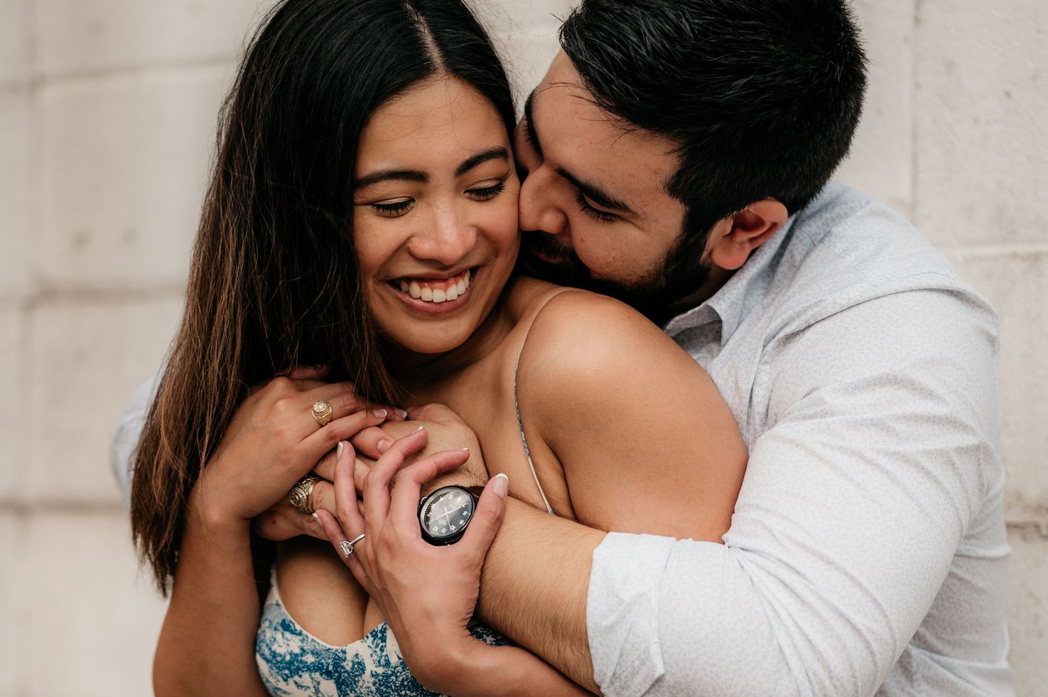 Candid engagement photo showing joyful couple embracing while displaying ring.
