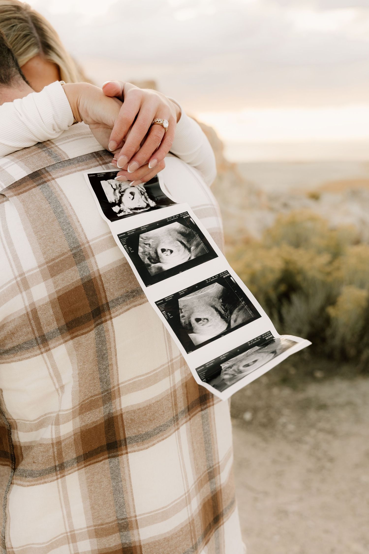 Hands holding ultrasound photos against a plaid blanket during sunset.