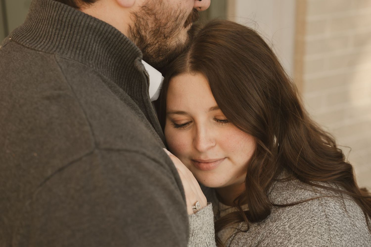 a woman with her eyes closed leaning into the chest of her husband while he looks off behind her