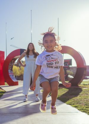 A child jumps joyfully in front of large red letters on a sunny day senior graduation portrait session