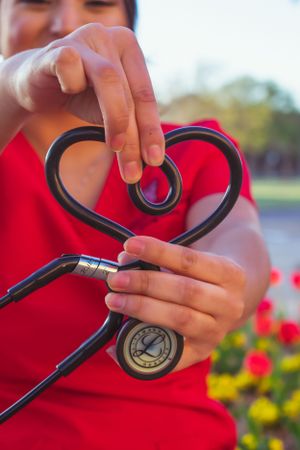 Hands shape a black stethoscope into a heart shape against a red shirt senior graduation portrait session