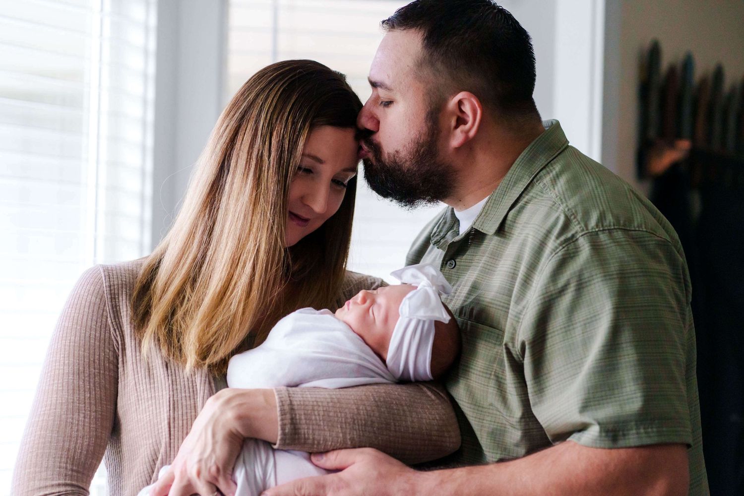 mom and dad hold baby girl by the window