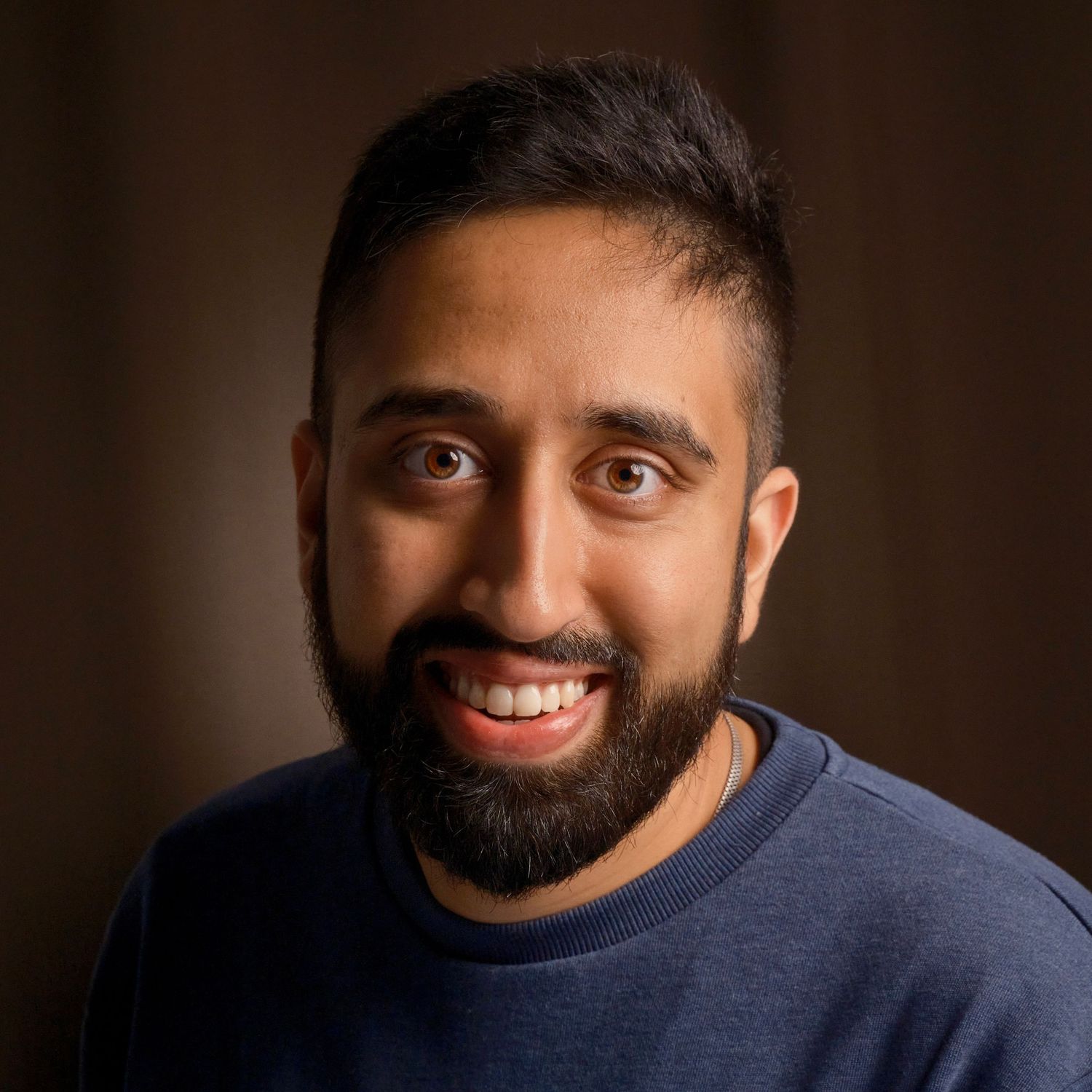 Studio portrait of person in blue sweater smiling against dark background.