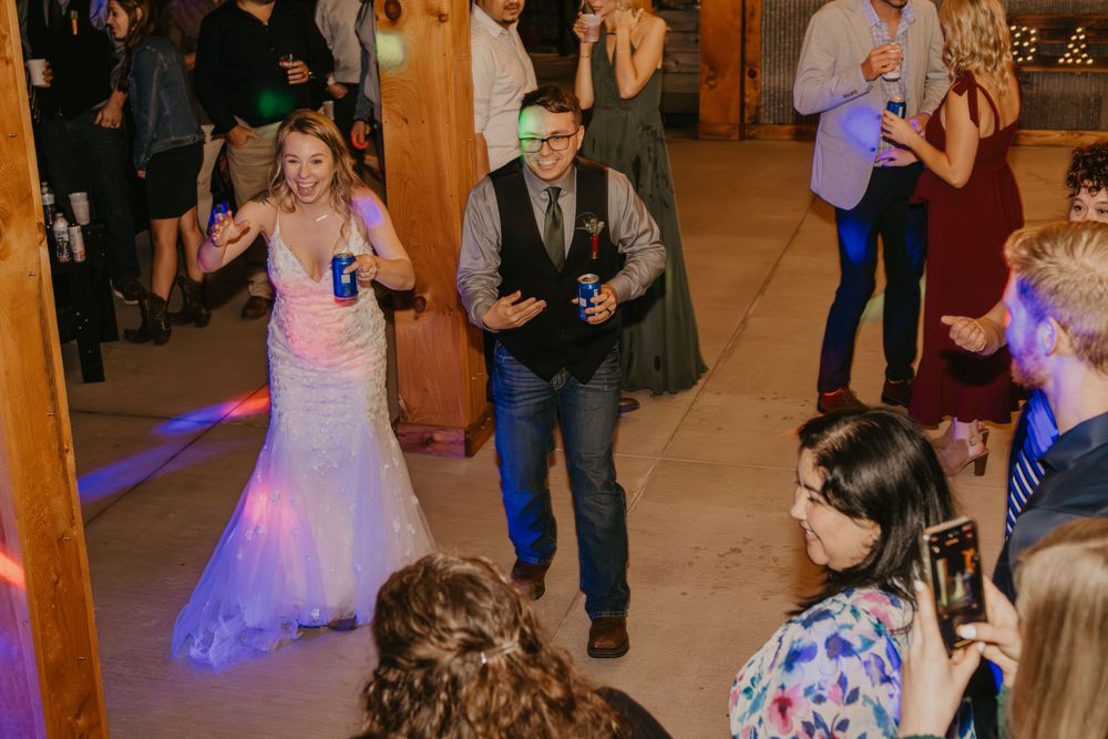 Bride and groom energetically enter wedding reception on dance floor in rustic barn venue.