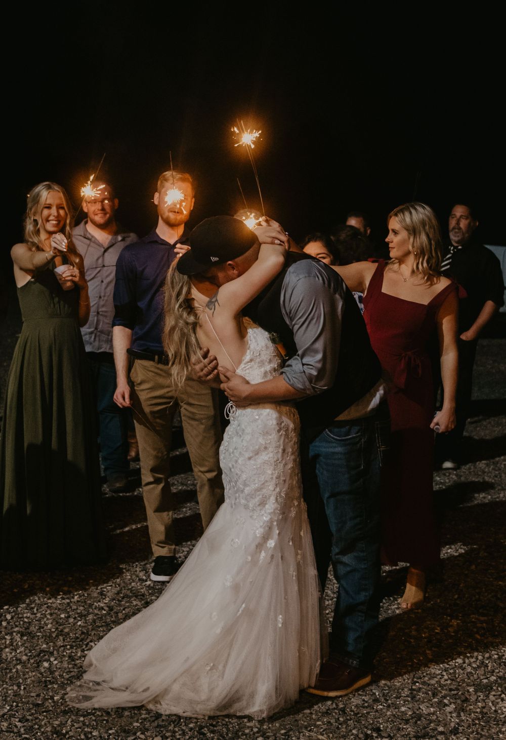 Bride and groom share a romantic kiss surrounded by guests holding sparklers at night.