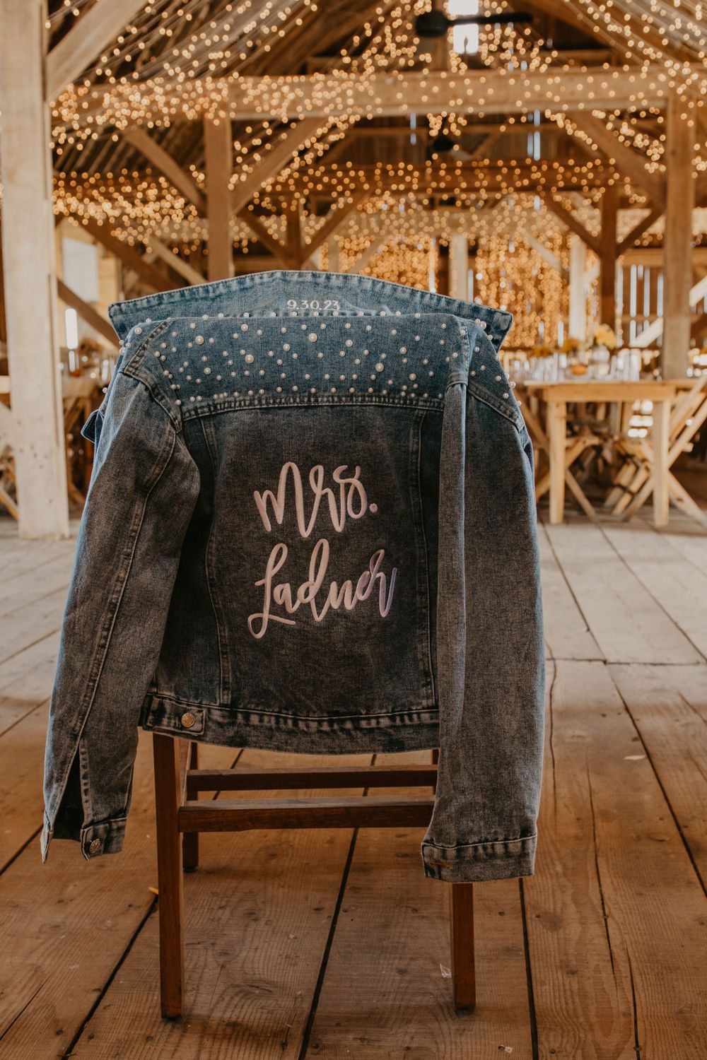Custom denim jacket with Mrs. Ladner painted on the back hanging in a fairy light barn.