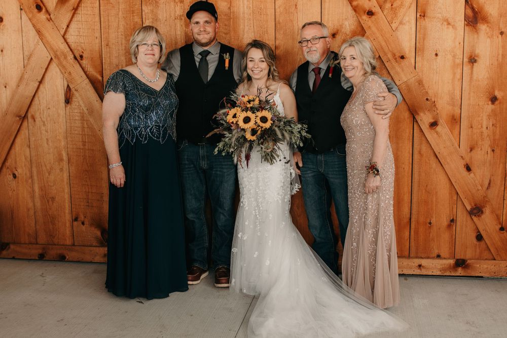 Wedding family portrait in front of wooden barn doors with bride holding sunflower bouquet.