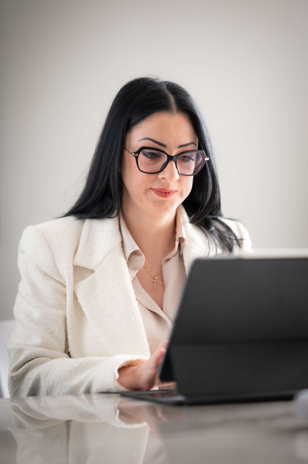 Business professional in white blazer working intently on laptop computer.