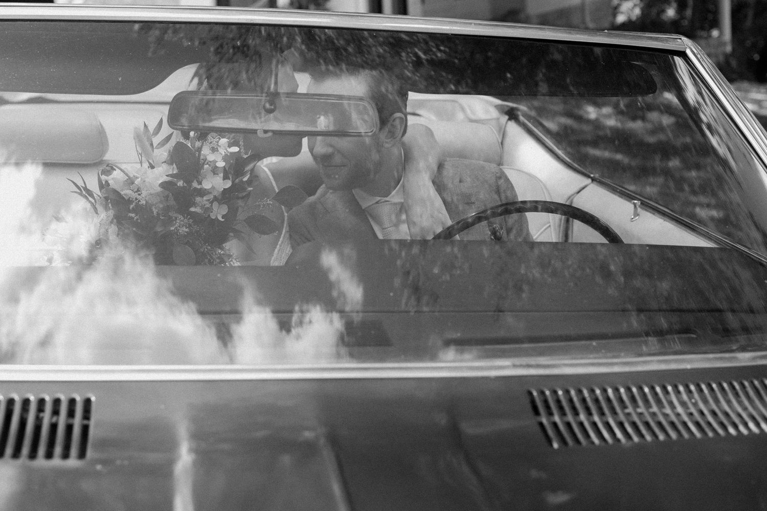 A vintage-style grayscale photo showing the reflection of a couple in a car windshield.