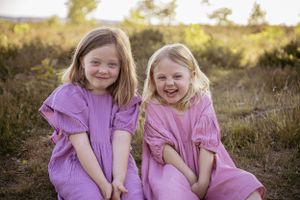 Two people wearing coordinated pink dresses laugh together in natural outdoor setting.