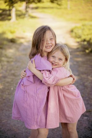 Sweet embrace between two people wearing pink and mauve dresses on sunny path.