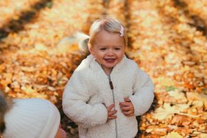 Child wearing cozy white jacket laughs while playing in autumn leaves.