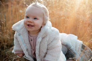 Happy baby in plush white coat playing outdoors during golden hour.