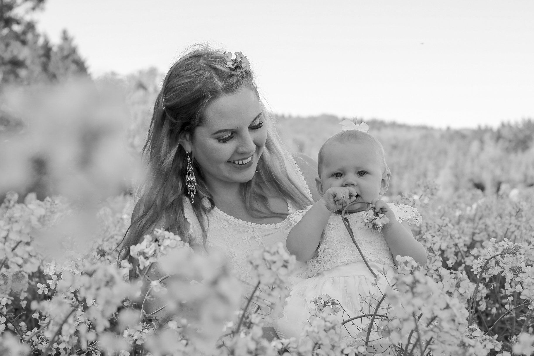 Mother and baby share tender moment among wildflowers in black and white photograph.