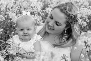 Black and white portrait of mother and baby in floral lace dresses amid blooming flowers.