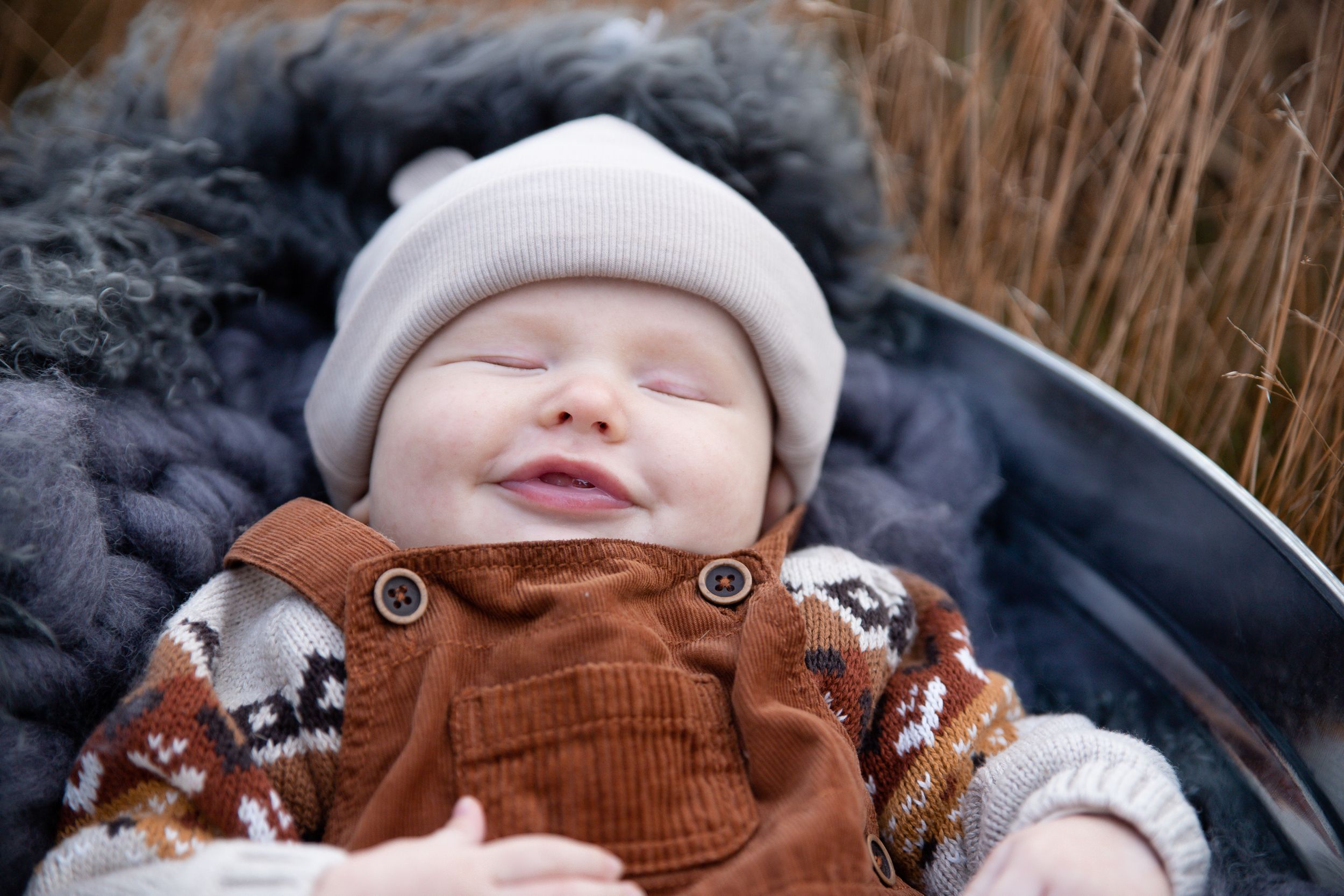 Sleeping baby wearing brown corduroy overalls and white winter hat outdoors.