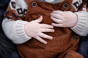 Close-up of small hands on brown corduroy overalls with white knit sleeves.