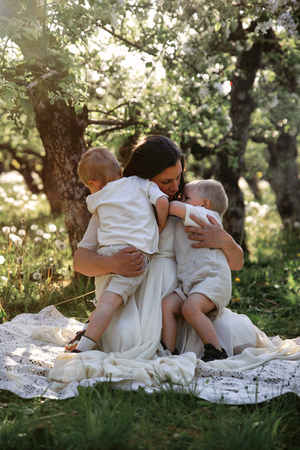Tender family moment captured in sunlit garden as parent embraces children on white blanket.