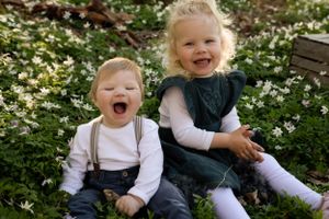 Two young children sit among blooming white flowers wearing coordinated outfits with suspenders.