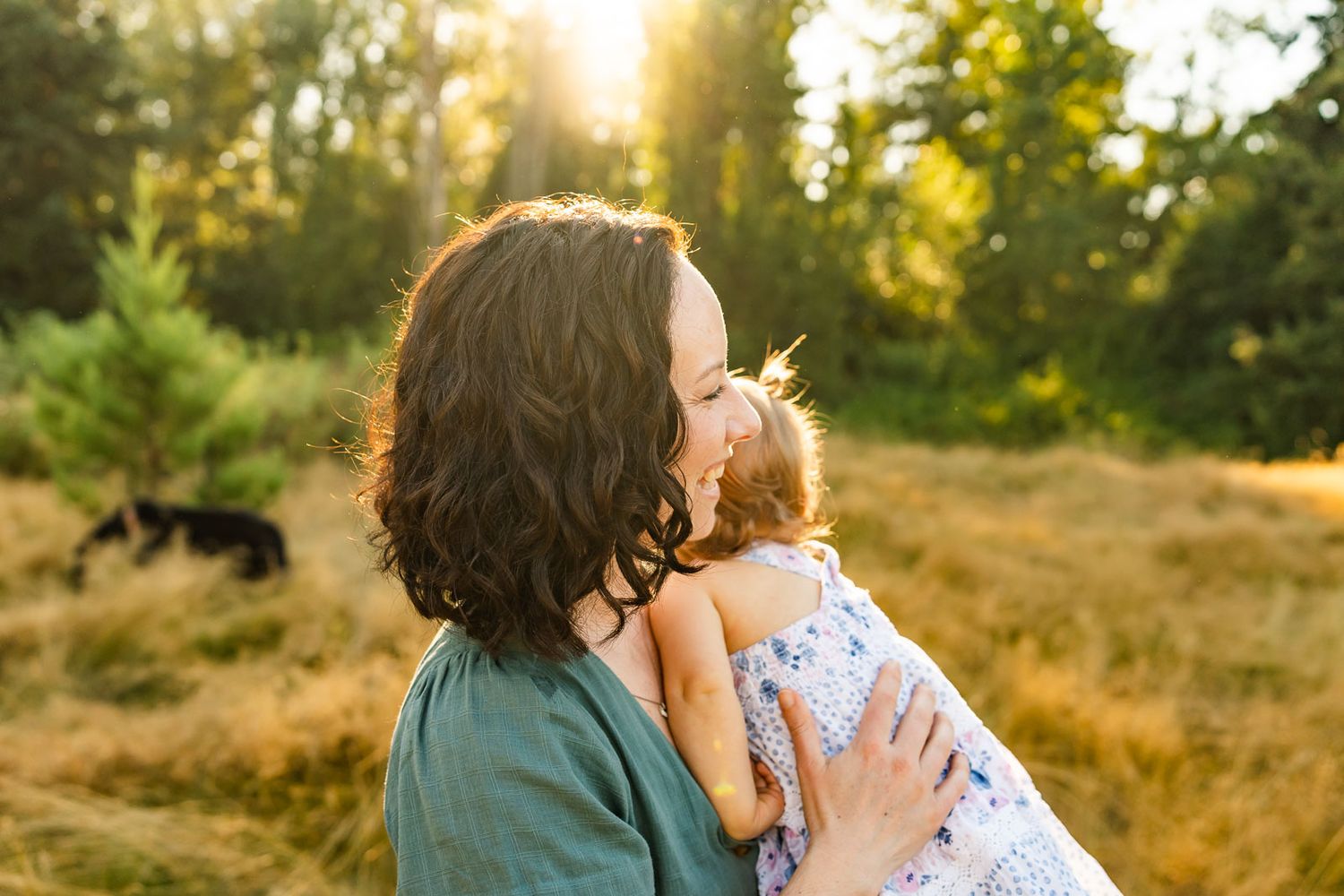 Mother snuggling her daughter, backlit in golden hour light.