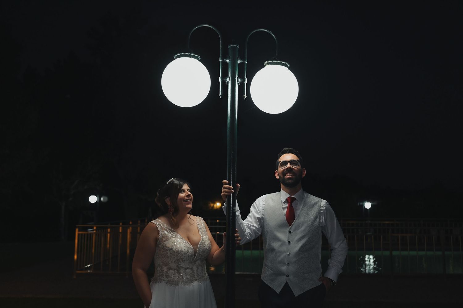 Wedding couple poses under vintage street lamp at night creating dramatic silhouette.