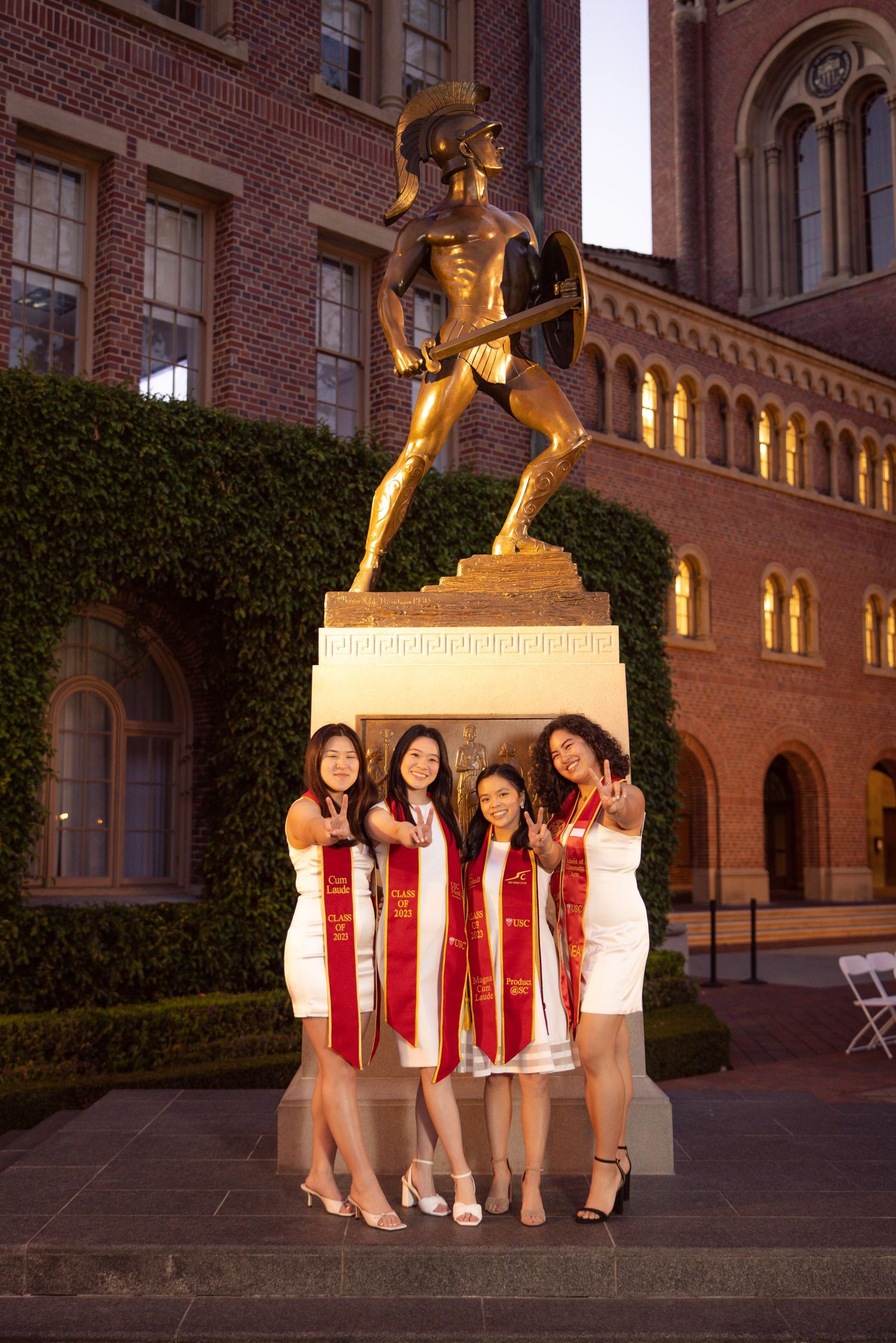 Graduation photo of four friends posing in front of Tommy Trojan statue at USC campus.