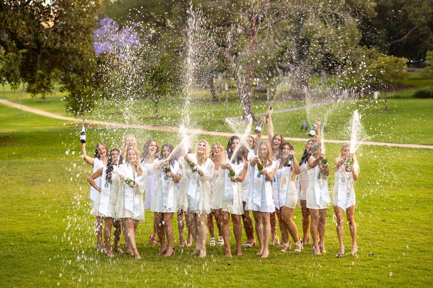 Celebration photo with water splashing over group in white dresses on green lawn.