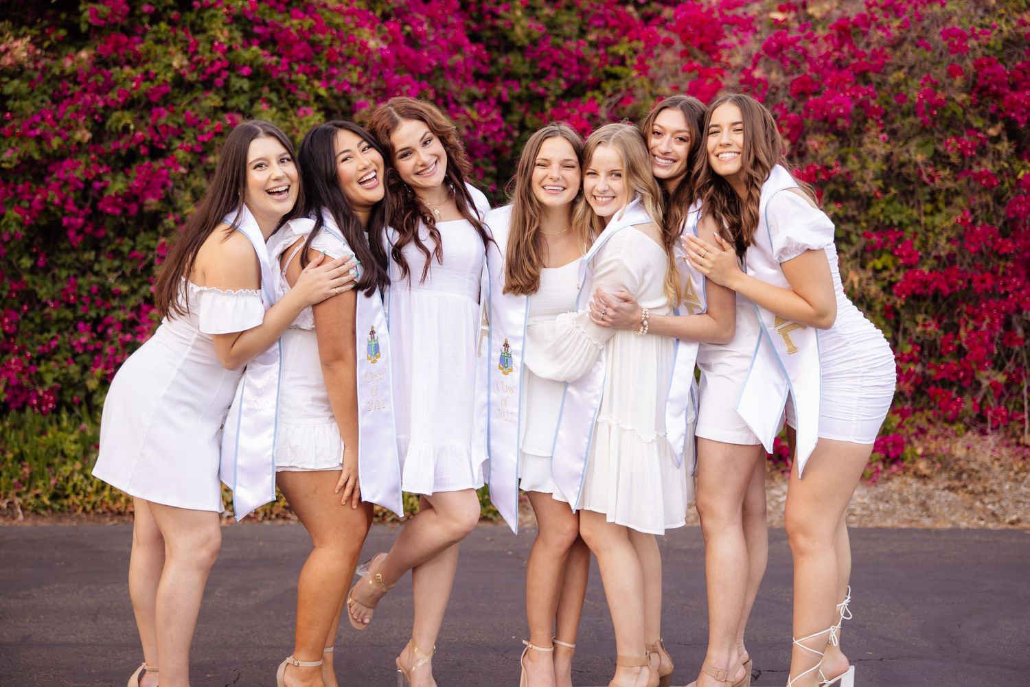Friends in white dresses pose together in front of vibrant pink bougainvillea flowers.