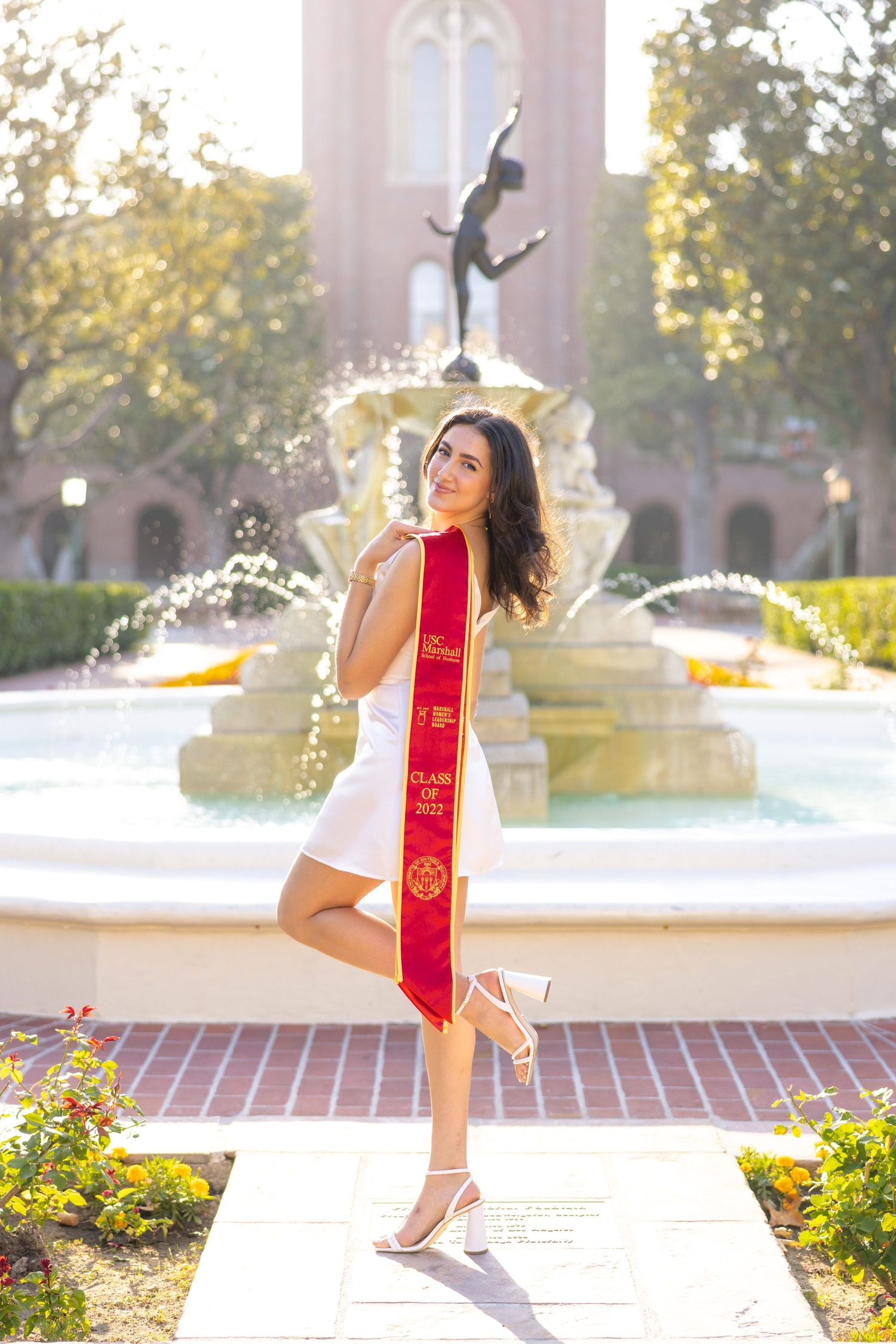 Graduate strikes playful pose by fountain wearing USC graduation stole.