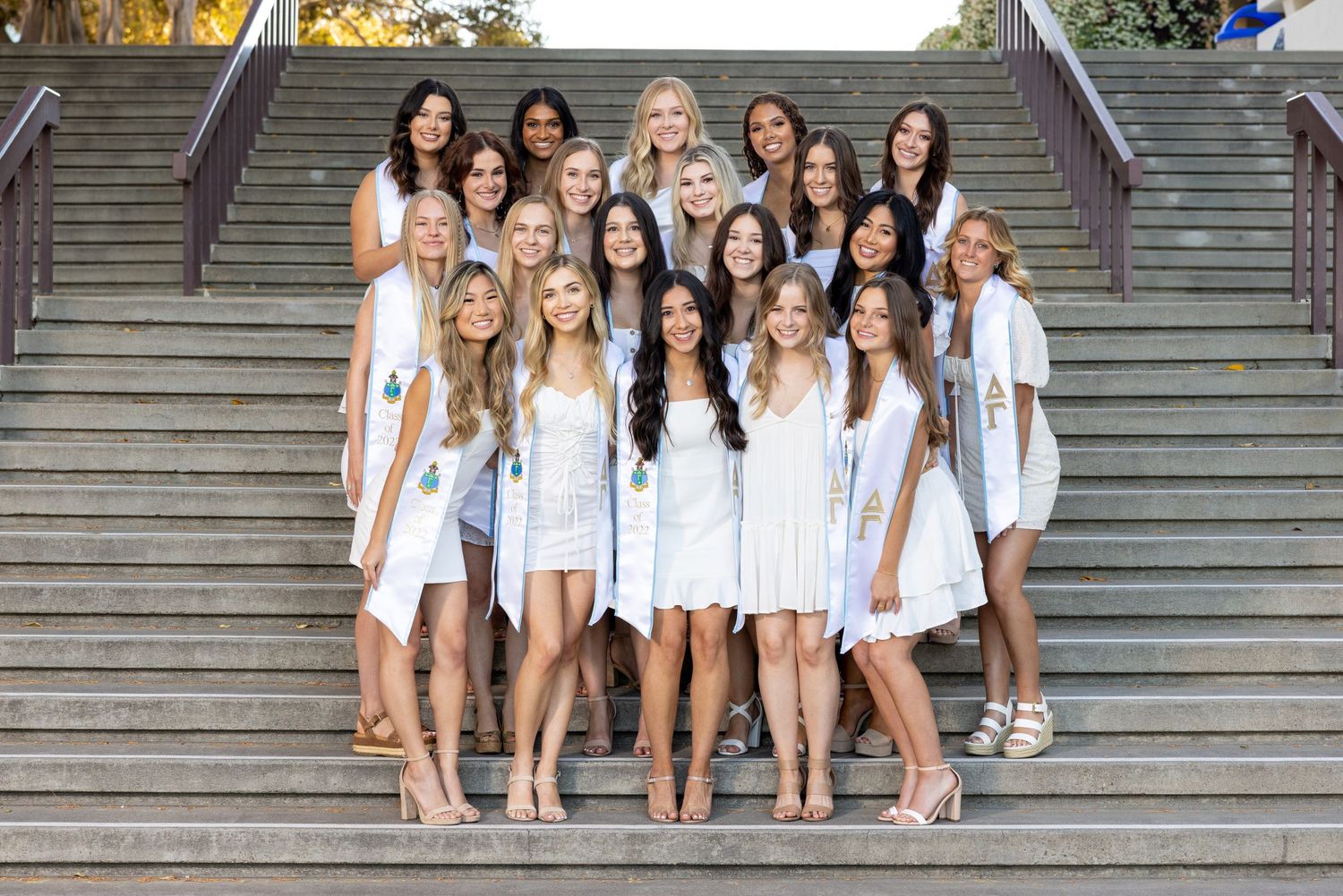 Group photo of graduates in white dresses arranged on stone steps.