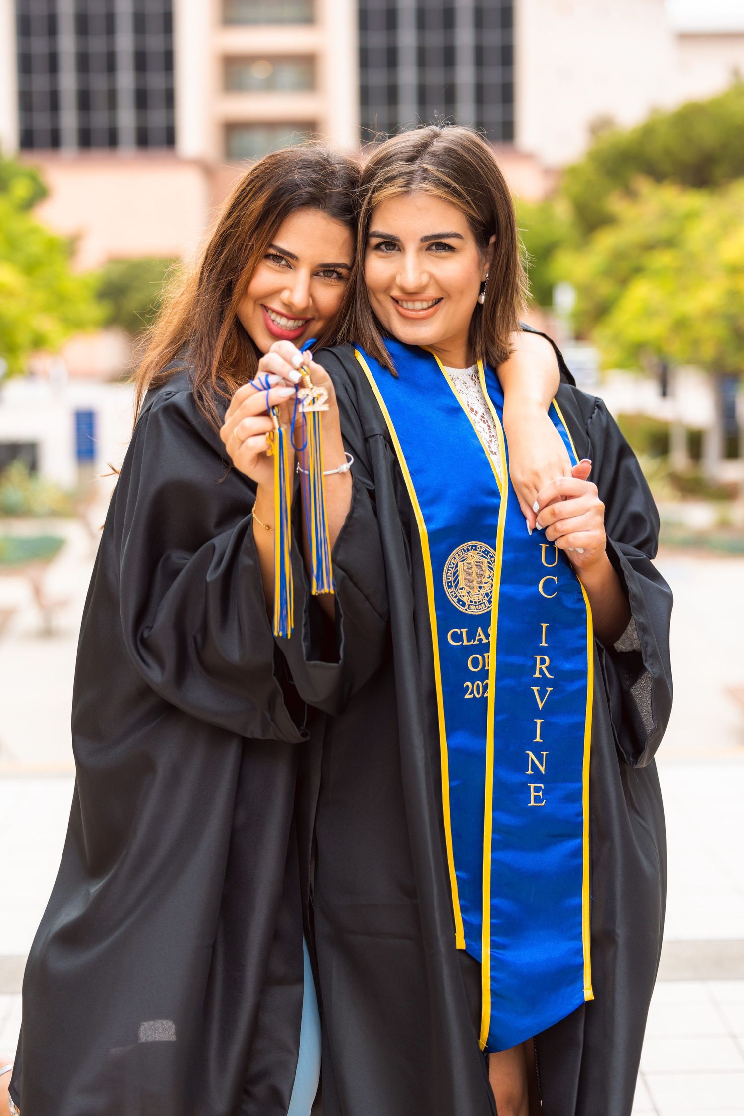 Two graduates hold their tassels while posing together in caps and gowns.