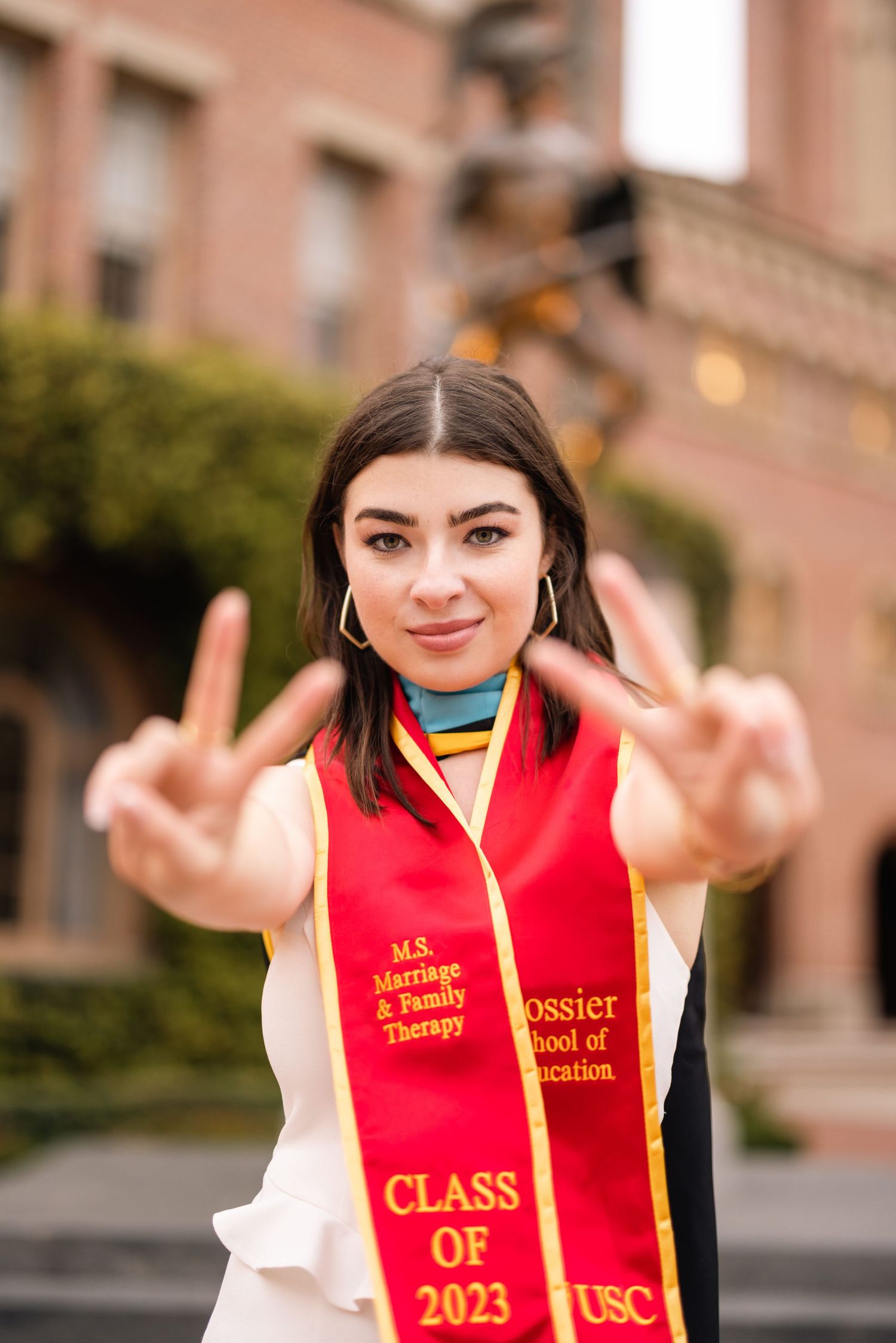 Graduate making peace signs while wearing red Class of 2023 graduation sash.
